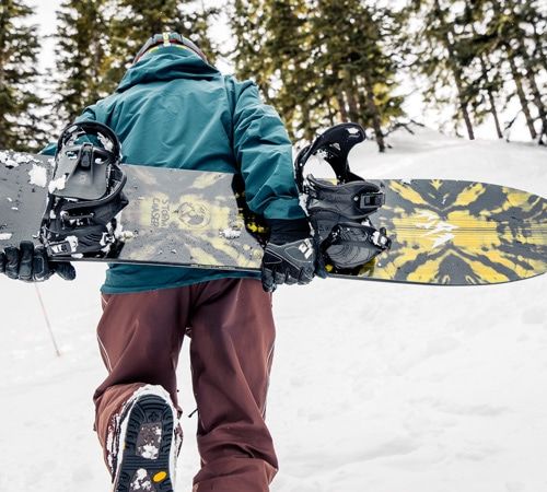 Snowboarder carrying a powder board up a hill