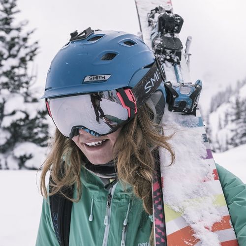 woman with ski goggles carrying skis